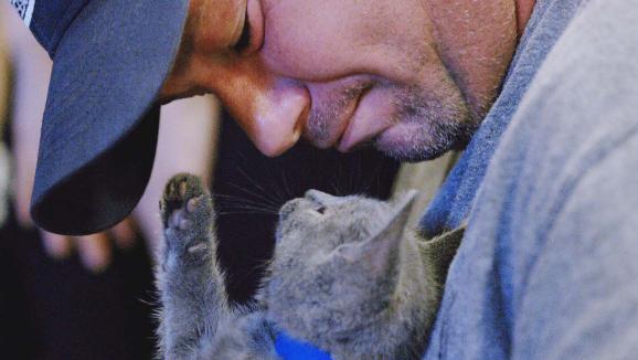 man wearing cap looks down at a kitten